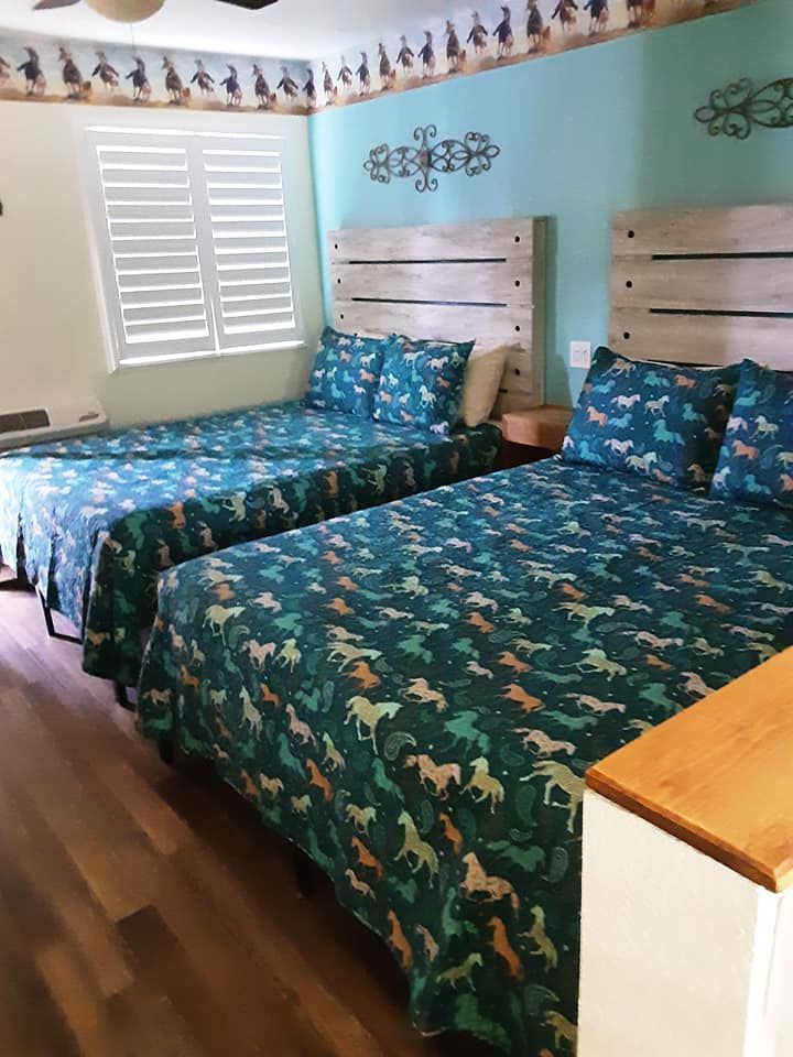 Two beds with teal horse-patterned bedding in a room with blue walls and wooden floors.