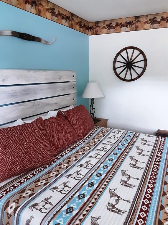 Bedroom with a cowboy theme, featuring a bed with horse print bedding, turquoise wall, and decorative wheel.