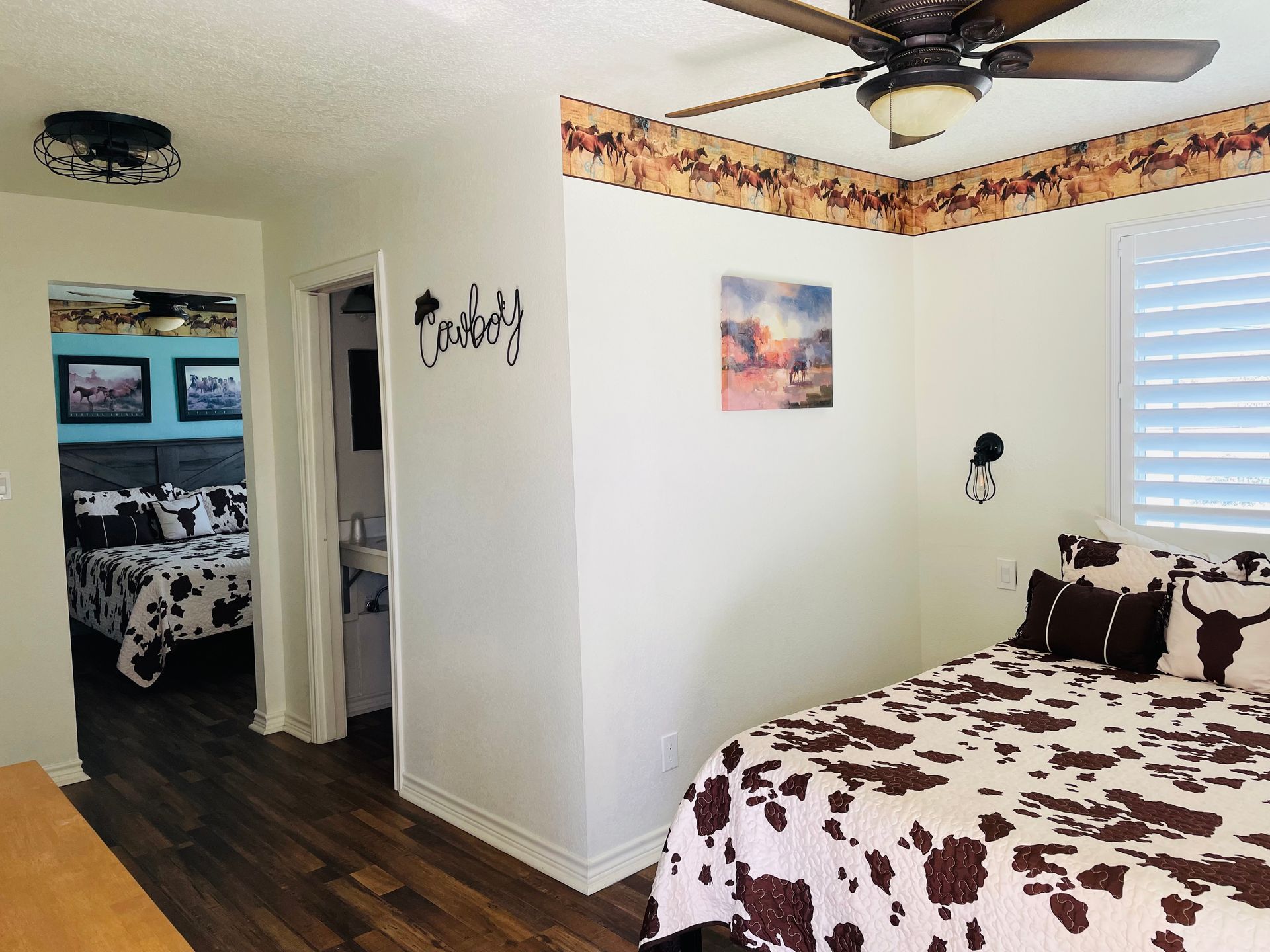Cow print bedding in a bedroom with wood floor and a second room visible, decorated with western themes.