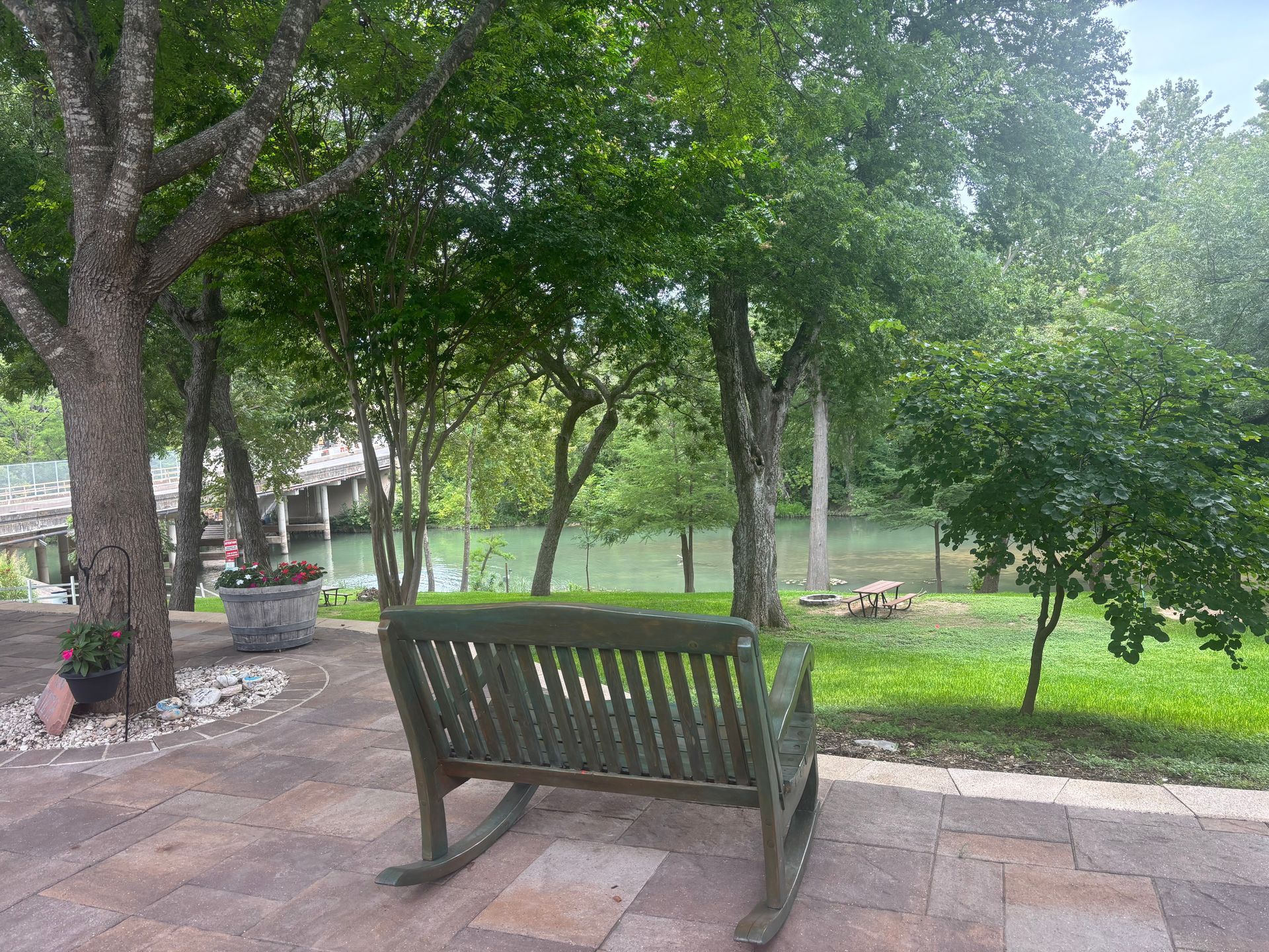 Green rocking chair on a patio overlooking a river, trees surrounding the area.