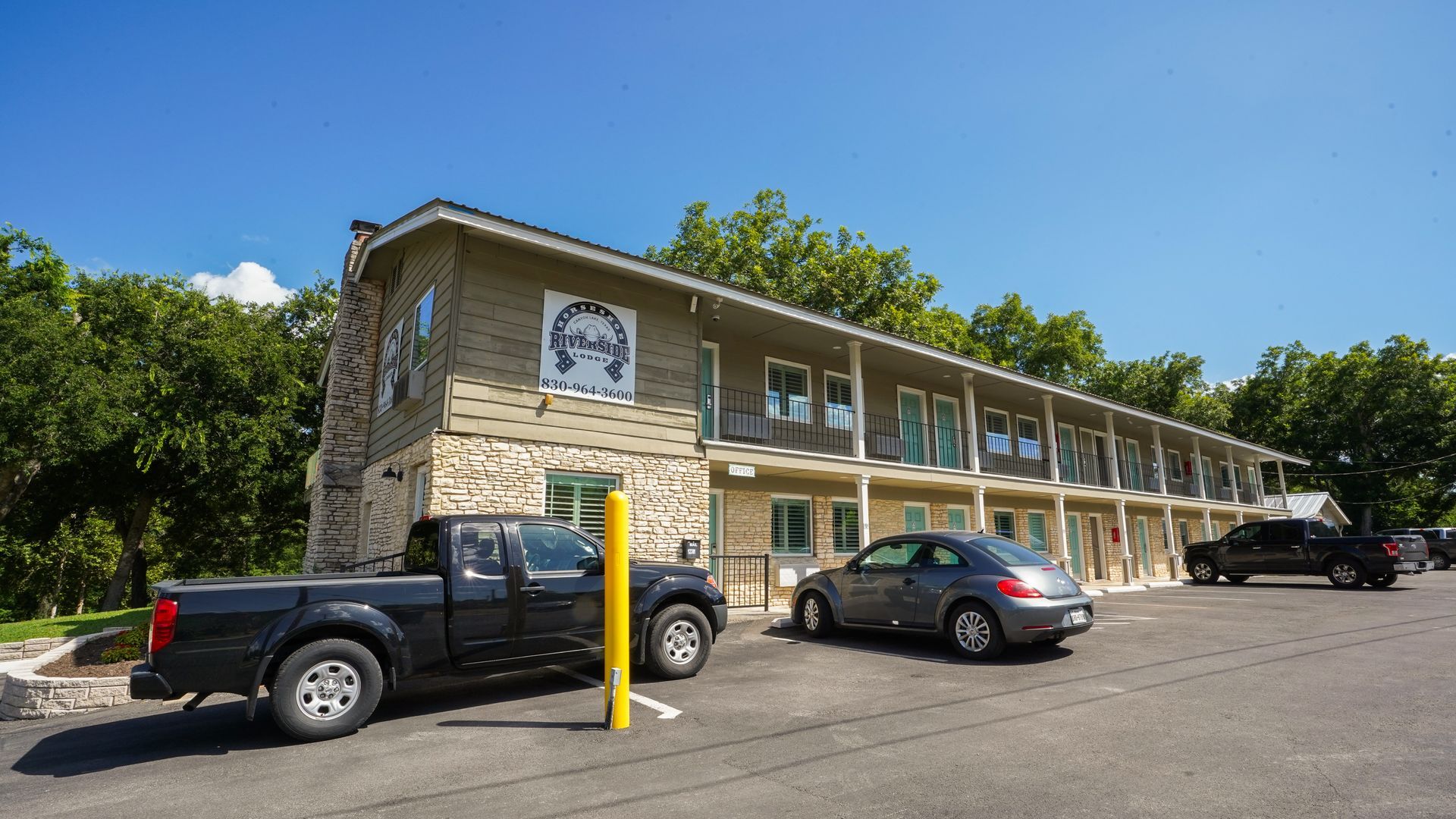 Motel exterior, two-story building with parked cars. Sunny day, trees visible.