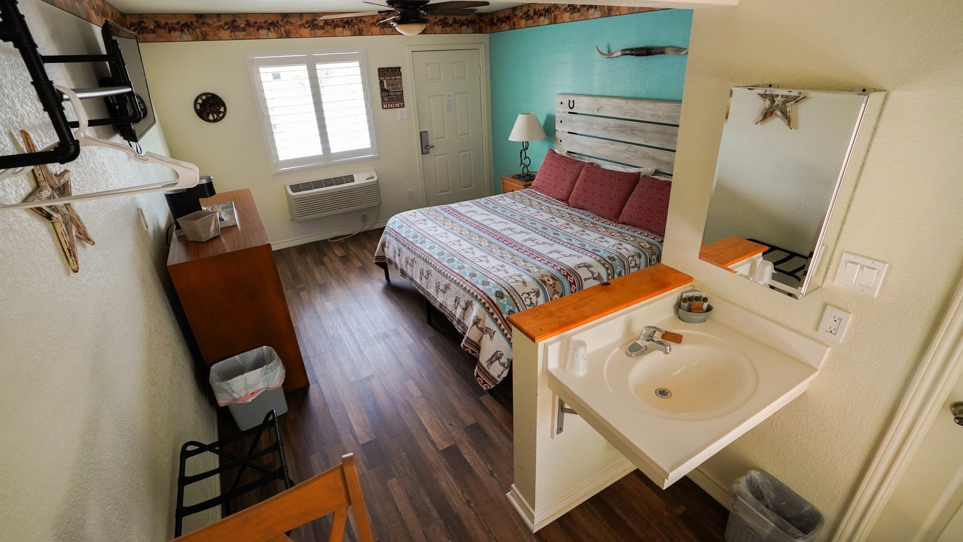 Small motel room with bed, vanity, and wood-look floors; turquoise wall behind the bed.