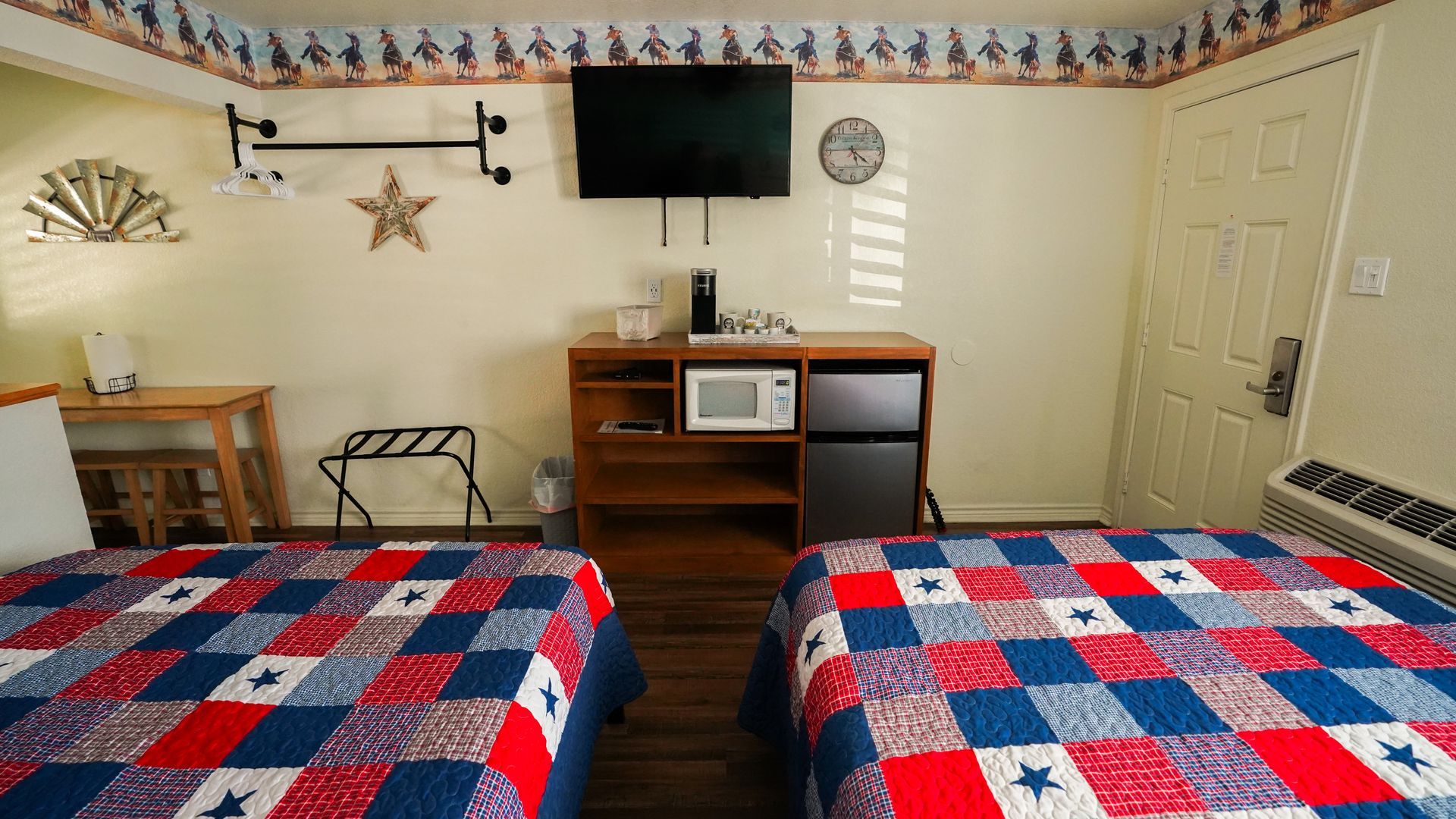 Two twin beds in a motel room, red, white, and blue quilt, TV, microwave, mini-fridge.