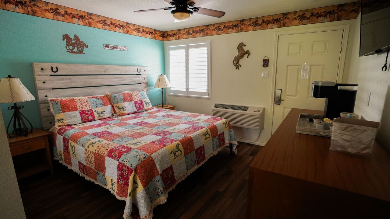 Bedroom with a bed, wooden headboard, colorful quilt, and small table with a lamp.