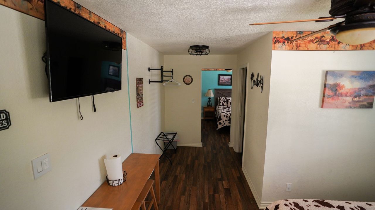 Hallway with TV, brown cabinets, and a view into a bedroom.
